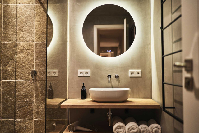 Boutique Apartment Flachsblüte - Badezimmer mit natürlichem Kalkspachtel gespachtelten Wänden mit rundem, großen Badspiegel mit warmer Beleuchtung (Photo 10)