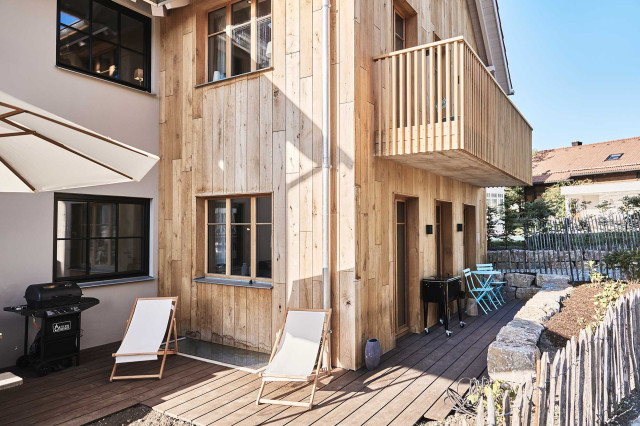 Das Flachshaus Ferienhaus - Ferienhaus mit Holzfassade, modernem Holzbalkon, sonniger Süd-Westterrasse aus Holz mit zwei weißen Liegestühlen, einem weißen Sonnenschirm und einem schwarzen Gasgrill (Photo 17)
