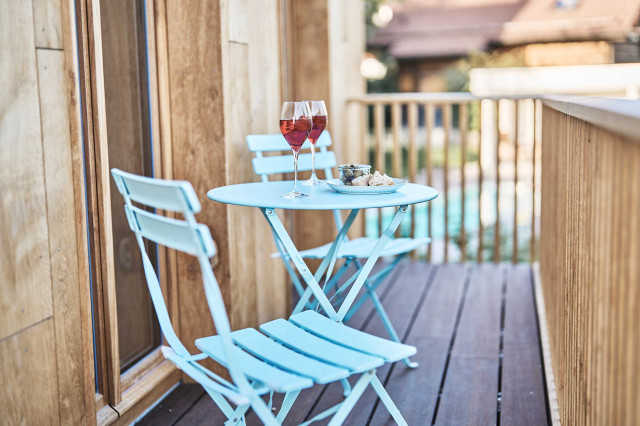 Das Flachshaus Ferienhaus - Moderner Holzbalkon mit zwei hellblauen Bistrostühlen und einem hellbblauen Bistrotisch, auf dem zwei Gläser Rotwein stehen (Photo 18)