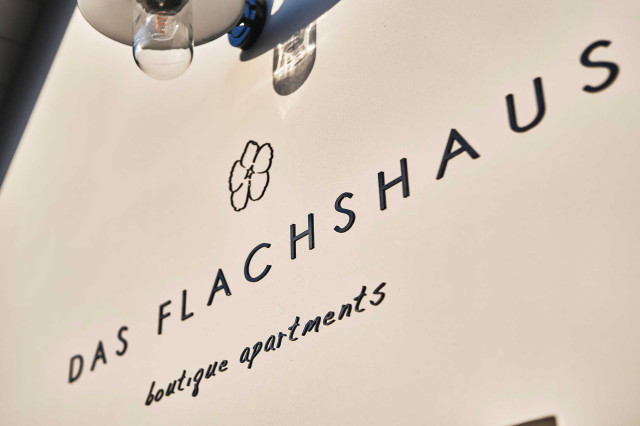 Das Flachshaus Ferienhaus - Ferienhaus Logo Das Flachshaus - Boutique Apartments an sonniger Hauswand mit nostalischer, schwarzer Wandlaterne (Photo 24)