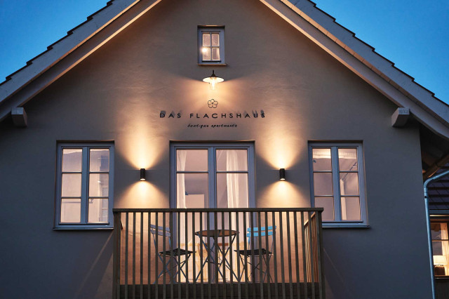 Das Flachshaus Ferienhaus - Warm beleuchtete Giebel-Fassade des Ferienhauses mit modernem Holzbalkon (Photo 25)