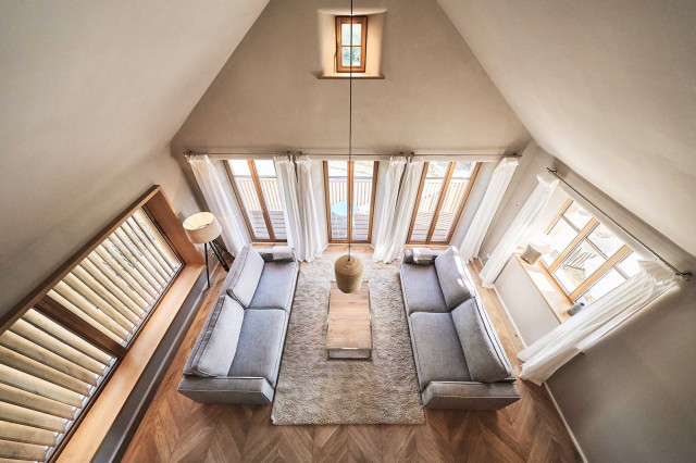 Das Flachshaus Ferienhaus - Wohnzimmer mit geöffnetem Giebel, zwei hellgrauen Sofas, Sprossenfenstern aus Holz, Panoramaverglasung mit Holzlamellen und Eiche-Fischgrät-Parkett (Photo 29)