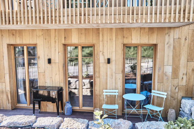 Boutique Apartment Flachsblüte - Holzfassade mit drei bodentiefen Holzsprossenfenstern, Holzterrasse, hellblauem Bistro-Set und schwarzem, mobilen, schwarzer Kühlbox mit vier Beinen und Rollen (Photo 22)