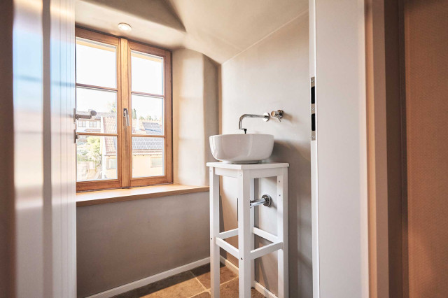 Das Flachshaus Ferienhaus - Gäste-WC mit Holzsprossenfenster, weißem kleinen Waschtischgestell aus Holz mit weißem runden Keramikwaschbecken und schlichter, verchromter Wandarmatur (Photo 45)