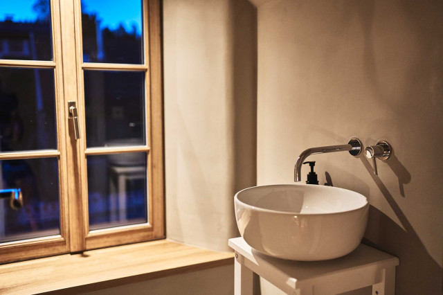 Boutique Apartment Bergfreuden - Kleines Gäste Wc mit warmer Beleuchtung, Holzsprossenfenster, weißem Waschtischgestell aus Holz und kleinem, runden Keramikwaschbecken (Photo 22)