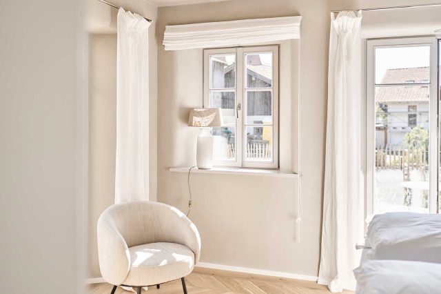 Boutique Apartment Flachsblüte - Helles Schlafzimmer mit weißen Sprossenfenstern und weißen Leinenvorhängen, hellbeigem, schlichtem Sessel und Eiche-Fischgrätparkett (Photo 1)