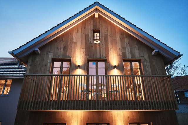 Boutique Apartment Bergfreuden - Ferienhaus mit moderner Holzfassade und Holzbalkon mit Sprossen bei abendlicher, warmer Beleuchtung durch schwarze Wandleuchten, die nach oben und unten abstrahlen. Durch die Sprossenfenster sind warm beleuchtete Innenräume zu sehen (Photo 24)