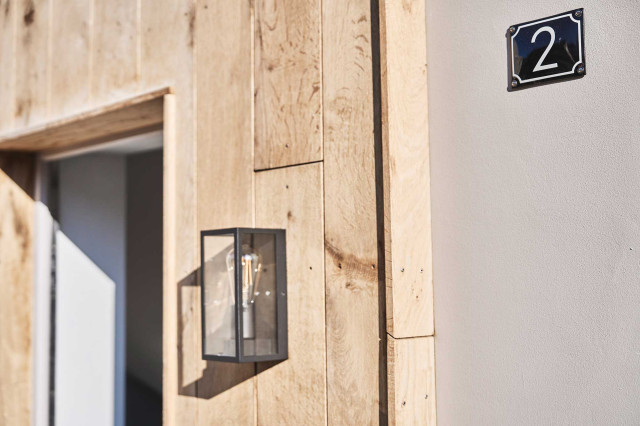 Das Flachshaus Ferienhaus - Haustür in moderner Holzfassade mit schlichter, geradliniger Wandlaterne mit Glas und filigranem Rahmen (Photo 53)