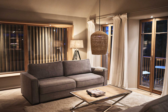 Das Flachshaus Ferienhaus - Warm beleuchtetes Wohnzimmer mit hellgrauem Sofa, vernickeltem Couchtischgestell mit Holztischplatte, Korbpendelleuchte, Tripod-Leuchte mit schwarzem Leuchtenfuß und hellem Lampenschirm, (Photo 54)