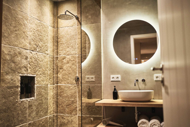 Boutique Apartment Flachsblüte - warm beleuchtetes Natursteinbad mit Regendusche, natürlich gespachteltem Kalkputz und rundem beleuchteten Badspiegel (Photo 37)