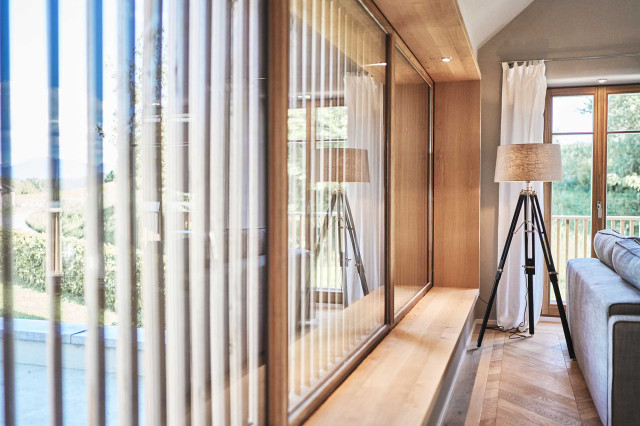 Boutique Apartment Bergfreuden - Wohnzimmer mit Panoramafenster und Holzlamellen, Eiche Fischgrätparkett, einem hellgrauen Sofa und einer Tripod Stehleuchte mit schwarzem Leuchtenfuß und beigem Leuchtenschirm (Photo 7)
