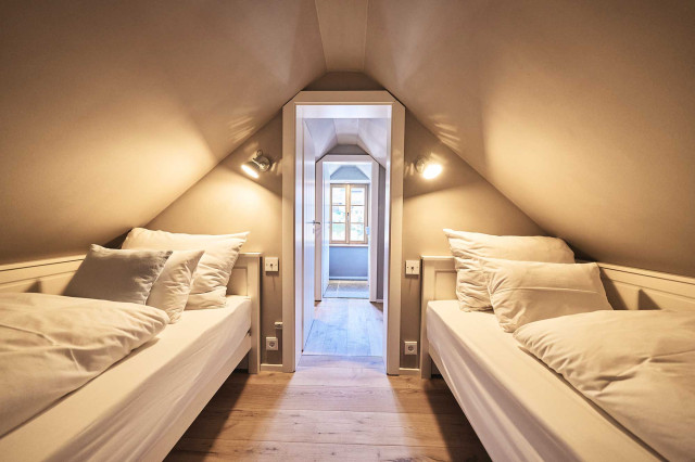 Boutique Apartment Bergfreuden - Hellgrau gestrichenes Giebelzimmer mit zwei weißen Alkoven aus Holz mit je einer weiß bezogenen, gefalteten Bettdecke und weißen aufgestellten Kissen (Photo 5)