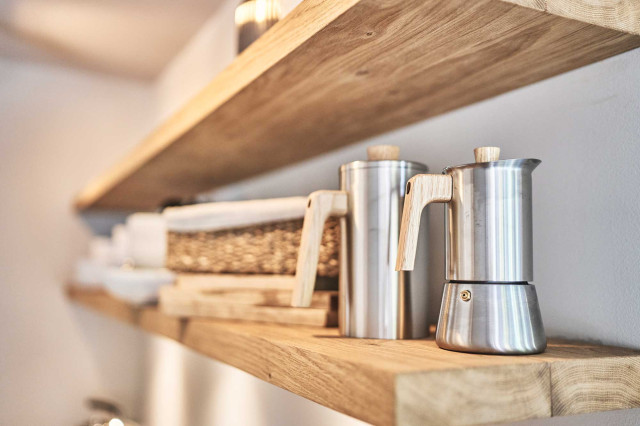 Boutique Apartment Bergfreuden - Zwei helle Regalböden aus Eichenholz mit Espressokocher und einer French Press aus mattem Edelstahl und Eichenholzgriff, dahinter ein geflochtener Brotkorb mit hellem Leinen-Inlay (Photo 35)
