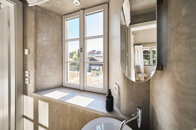 Boutique Apartment Bergfreuden - Badezimmer mit natürlichem, grauem Kalkputz gespachtelten Wänden und abgerundeten Fensterlaibungen, weißen Sprossenfenster und ovalem Spiegel, in dem sich ein Polsterstuhl im Chesterfield Design spiegelt (Photo 36)