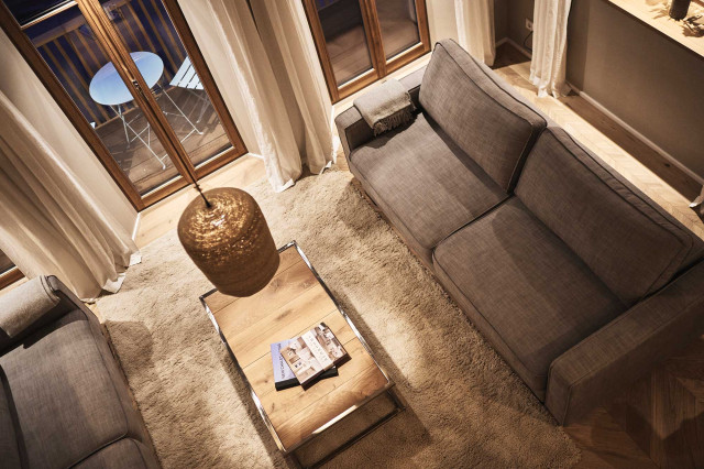 Boutique Apartment Bergfreuden - Wohnzimmer mit warmer Beleuchtung mit zwei Sofas, flauschigem Teppich einem Sofatisch mit hellen Holzdielen, Holzsprossenfenstern mit weißen Leinenvorhängen (Photo 43)